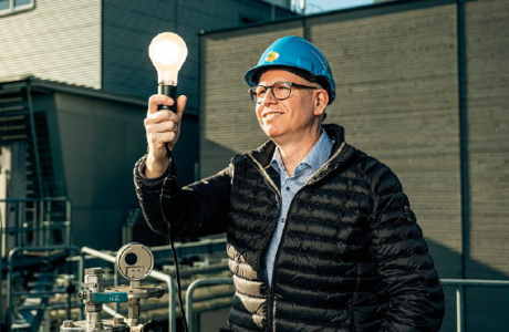 Patrik Feusi, Geschäftsführer Limeco, steht auf dem Dach der Faultürme und hält eine leuchtende Glühbirne in der Hand und symbolisiert damit die Vision von sauberer Energie aus Abfall und Abwasser.